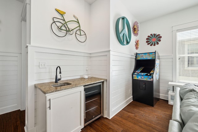 kitchen featuring a sink, light stone countertops, wine cooler, white cabinets, and dark wood-style flooring