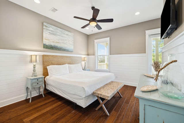 bedroom with dark wood finished floors, multiple windows, visible vents, and a wainscoted wall