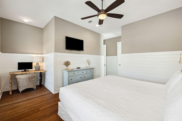 bedroom with a wainscoted wall, visible vents, dark wood finished floors, and a ceiling fan