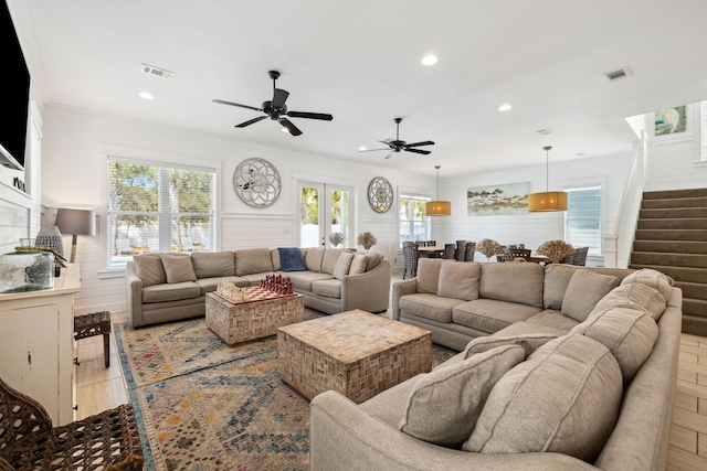 living area featuring stairs, visible vents, ornamental molding, and a ceiling fan