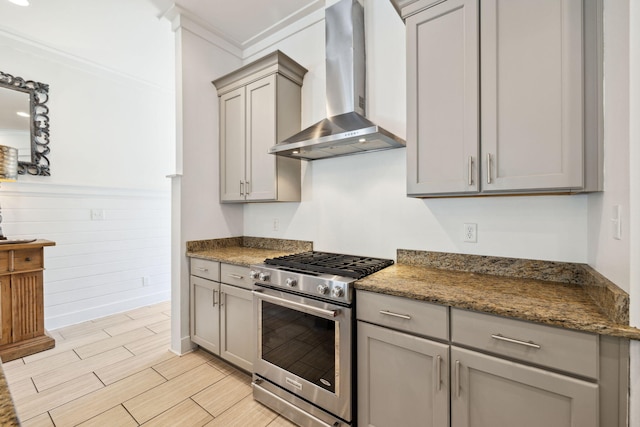 kitchen featuring wood finish floors, gray cabinets, high end stove, crown molding, and wall chimney range hood