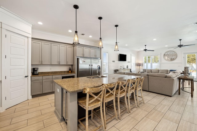 kitchen with light stone countertops, a breakfast bar, a sink, gray cabinetry, and built in refrigerator