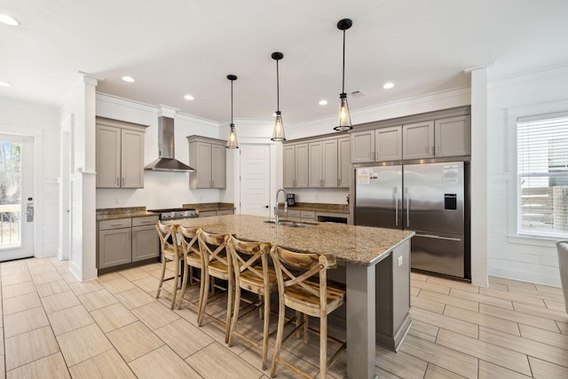 kitchen with wall chimney range hood, a breakfast bar, built in refrigerator, gray cabinets, and a sink