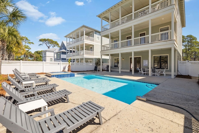 rear view of house with a fenced backyard, a balcony, a pool with connected hot tub, and a patio