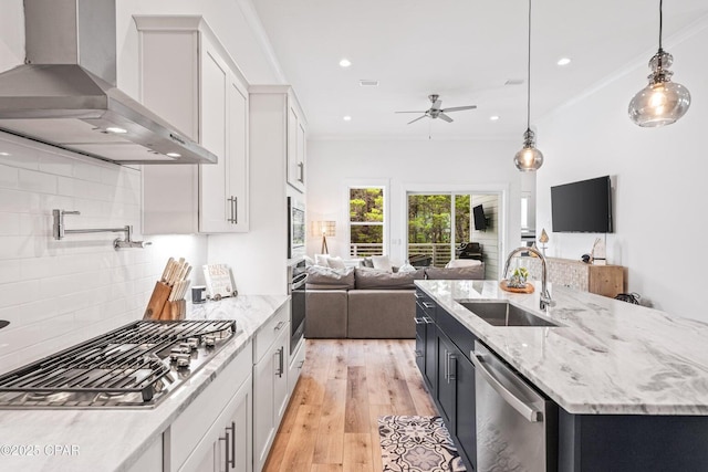 kitchen with ceiling fan, a sink, appliances with stainless steel finishes, wall chimney range hood, and open floor plan