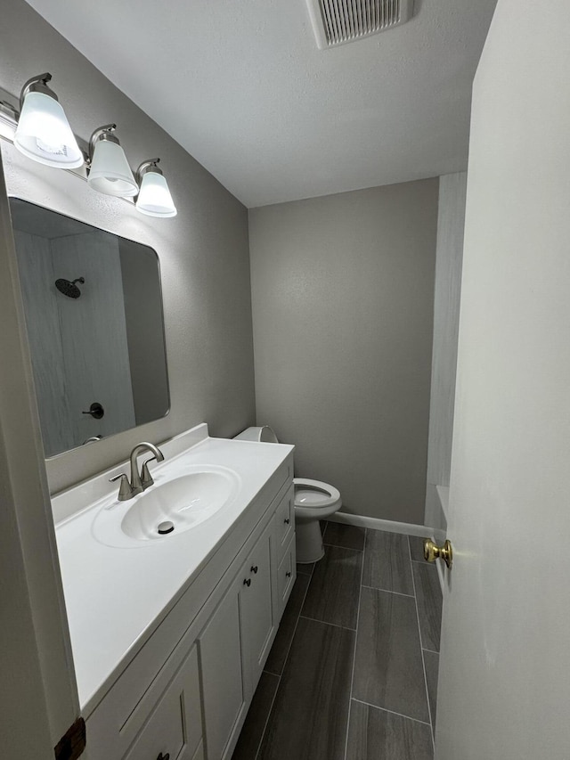 bathroom featuring vanity, baseboards, visible vents, walk in shower, and toilet