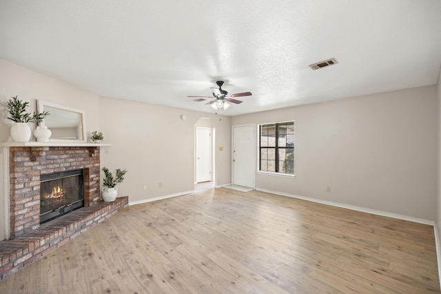 unfurnished living room featuring wood finished floors, baseboards, visible vents, a fireplace, and ceiling fan