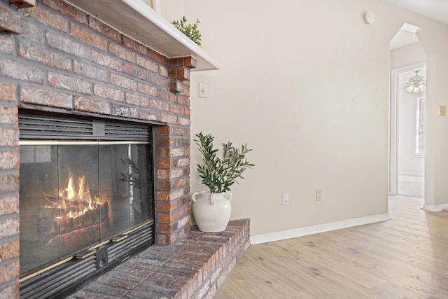 room details with arched walkways, a brick fireplace, baseboards, and wood finished floors