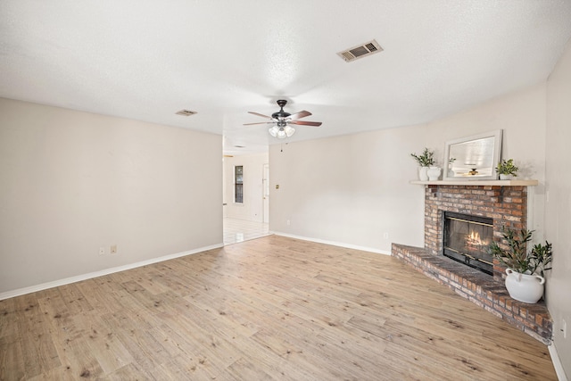 unfurnished living room featuring wood finished floors, baseboards, visible vents, a fireplace, and ceiling fan