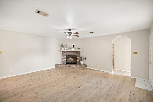 unfurnished living room featuring visible vents, a brick fireplace, ceiling fan, light wood-style floors, and arched walkways