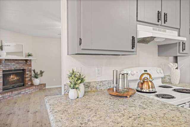 kitchen featuring wood finished floors, white range with electric cooktop, gray cabinets, under cabinet range hood, and a brick fireplace