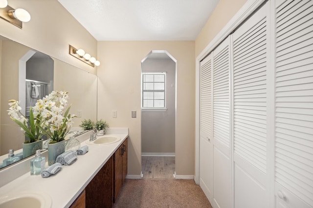 bathroom with a sink, a closet, baseboards, and double vanity