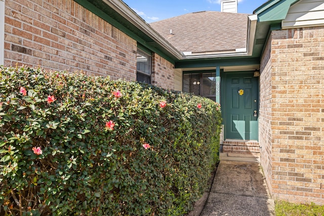 property entrance with brick siding, roof with shingles, and a chimney