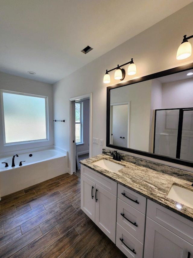 bathroom with double vanity, wood finish floors, a garden tub, and a sink