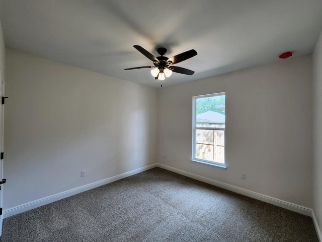 spare room featuring baseboards, dark carpet, and a ceiling fan