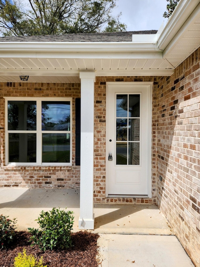 entrance to property with brick siding and roof with shingles