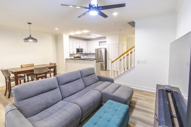 living area with stairway, light wood-style flooring, a ceiling fan, and ornamental molding