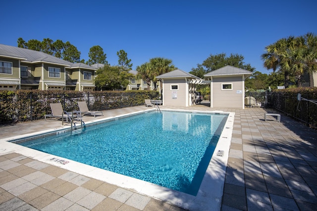 pool featuring a storage unit, an outdoor structure, a patio, and fence