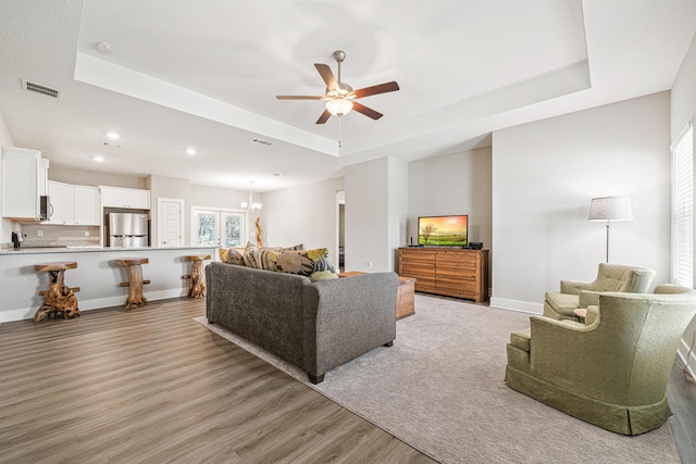 living room featuring visible vents, baseboards, light wood-style floors, a raised ceiling, and a ceiling fan