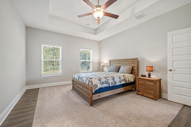 bedroom with a ceiling fan, wood finished floors, baseboards, visible vents, and a tray ceiling