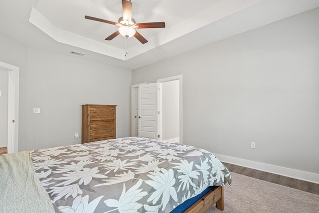 bedroom with visible vents, baseboards, wood finished floors, a raised ceiling, and a ceiling fan