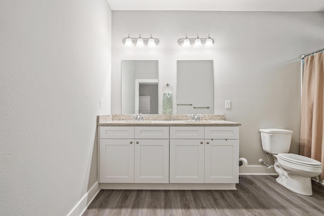 full bathroom featuring toilet, a sink, wood finished floors, double vanity, and baseboards