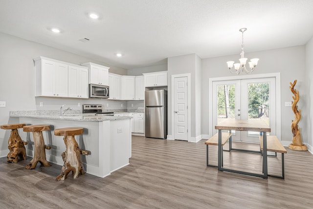 kitchen featuring a chandelier, white cabinetry, stainless steel appliances, and light wood-type flooring