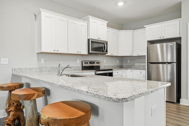 kitchen with appliances with stainless steel finishes, white cabinetry, a peninsula, and a sink