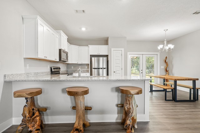 kitchen with a peninsula, wood finished floors, visible vents, and stainless steel appliances