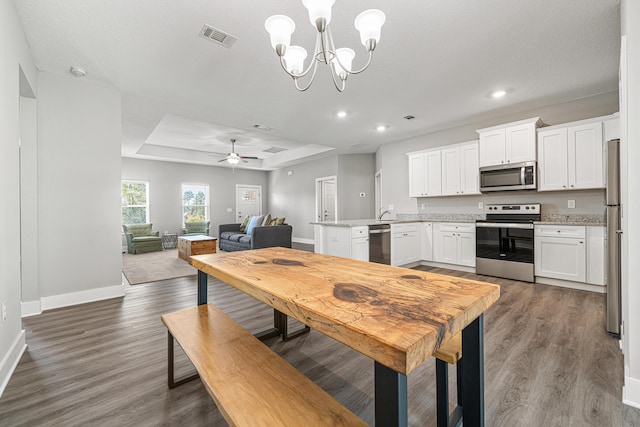 dining room featuring baseboards, visible vents, dark wood finished floors, a raised ceiling, and ceiling fan with notable chandelier