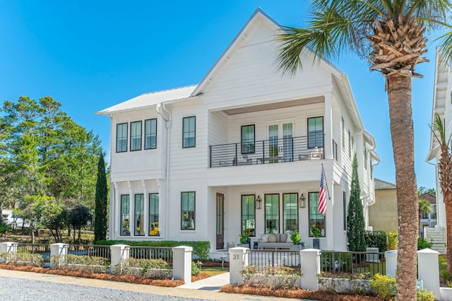 view of front of home featuring a balcony, a standing seam roof, covered porch, a fenced front yard, and metal roof