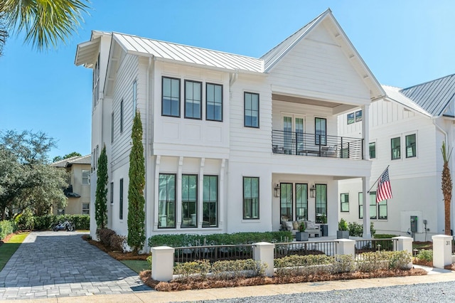 view of front facade with a fenced front yard, central AC unit, metal roof, a balcony, and a standing seam roof