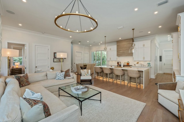 living area featuring a notable chandelier, visible vents, light wood-type flooring, and ornamental molding