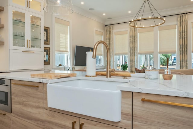 kitchen with a notable chandelier, a sink, crown molding, stainless steel oven, and light stone countertops