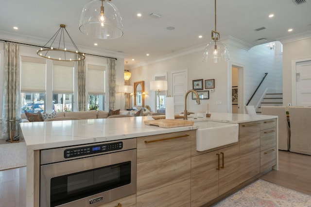 kitchen featuring light wood finished floors, a sink, crown molding, modern cabinets, and open floor plan