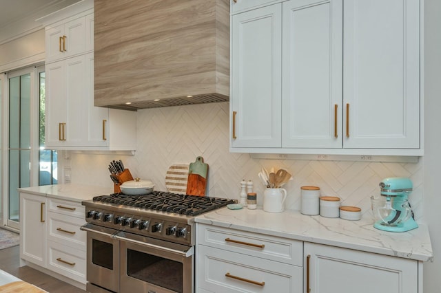 kitchen featuring custom range hood, light stone counters, double oven range, backsplash, and white cabinetry