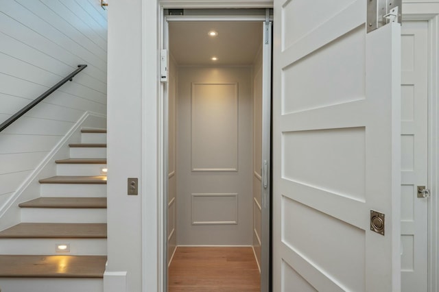 stairway with elevator, recessed lighting, and wood finished floors