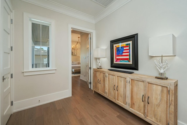 corridor with visible vents, crown molding, baseboards, wood finished floors, and a notable chandelier