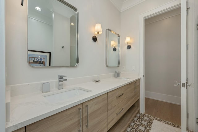 bathroom with wood finished floors, baseboards, double vanity, ornamental molding, and a sink