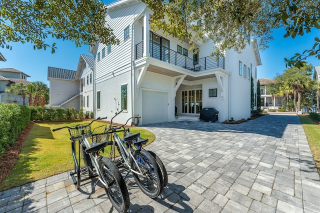 rear view of house featuring a balcony, a yard, an attached garage, stucco siding, and decorative driveway