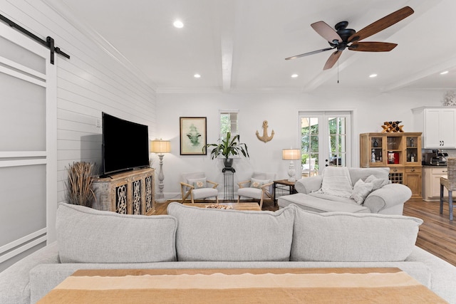 living area featuring beamed ceiling, a barn door, recessed lighting, wood finished floors, and a ceiling fan