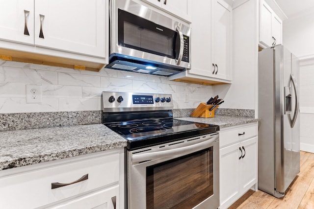 kitchen with light wood-type flooring, backsplash, appliances with stainless steel finishes, and white cabinetry