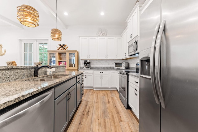 kitchen with a sink, light stone countertops, appliances with stainless steel finishes, and white cabinetry