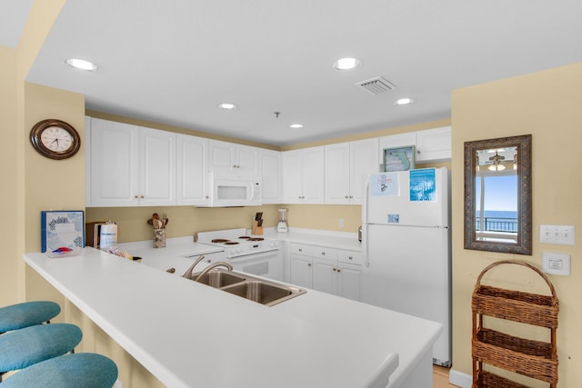 kitchen featuring visible vents, a sink, a kitchen breakfast bar, white appliances, and a peninsula