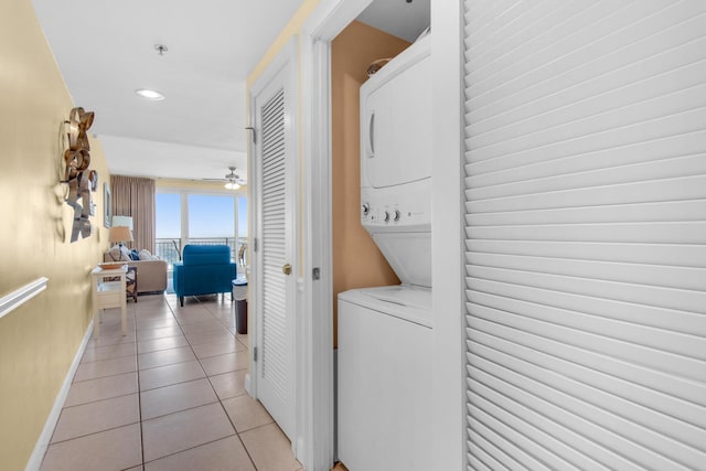 washroom with a ceiling fan, baseboards, stacked washing maching and dryer, laundry area, and light tile patterned flooring