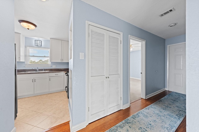 hall featuring visible vents, light wood-style flooring, baseboards, and a sink