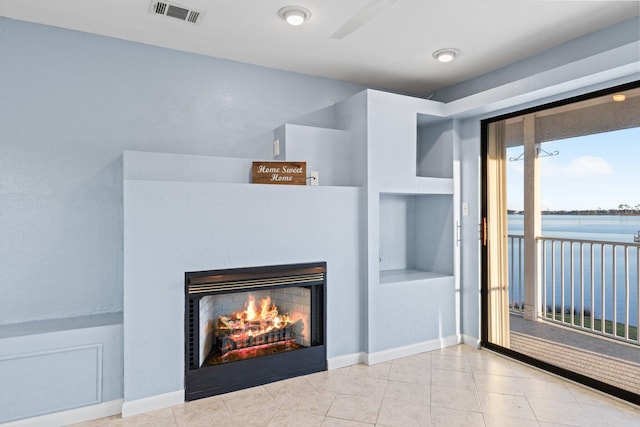 unfurnished living room with tile patterned flooring, visible vents, baseboards, a water view, and a warm lit fireplace