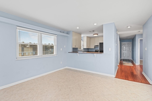 kitchen with baseboards, a breakfast bar, recessed lighting, freestanding refrigerator, and dark countertops