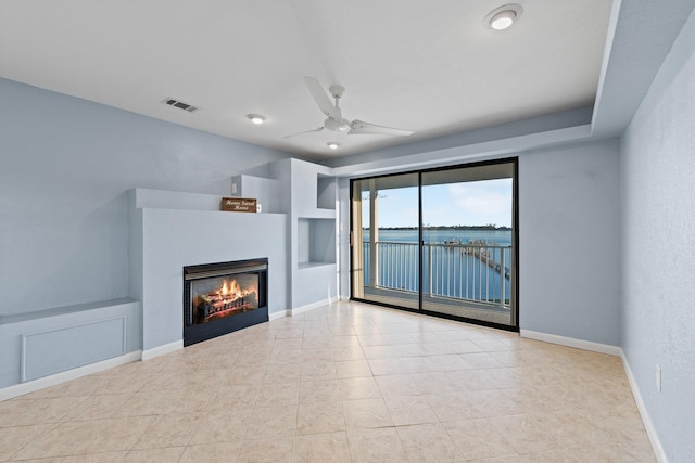 unfurnished living room with visible vents, baseboards, a water view, a glass covered fireplace, and a ceiling fan