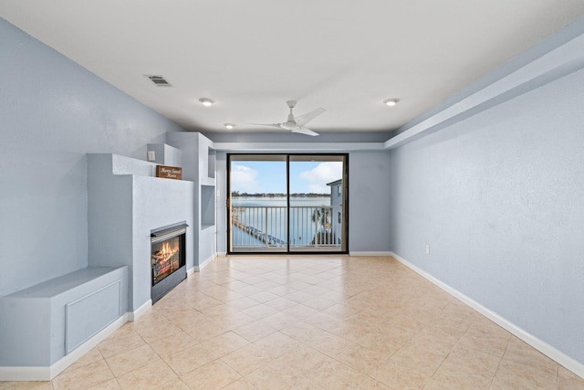 unfurnished living room featuring visible vents, a water view, a ceiling fan, a glass covered fireplace, and baseboards